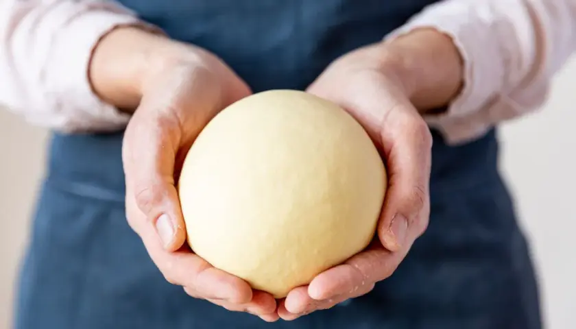 Hände halten einen glatten, gelben Ball aus nudelteig ohne ei.