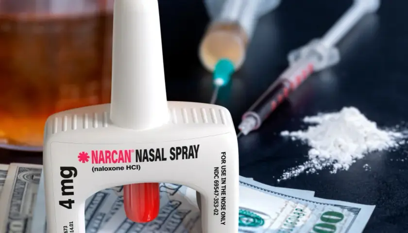 Nasalny spray nalokson, strzykawki i biały proszek na tle banknotów.