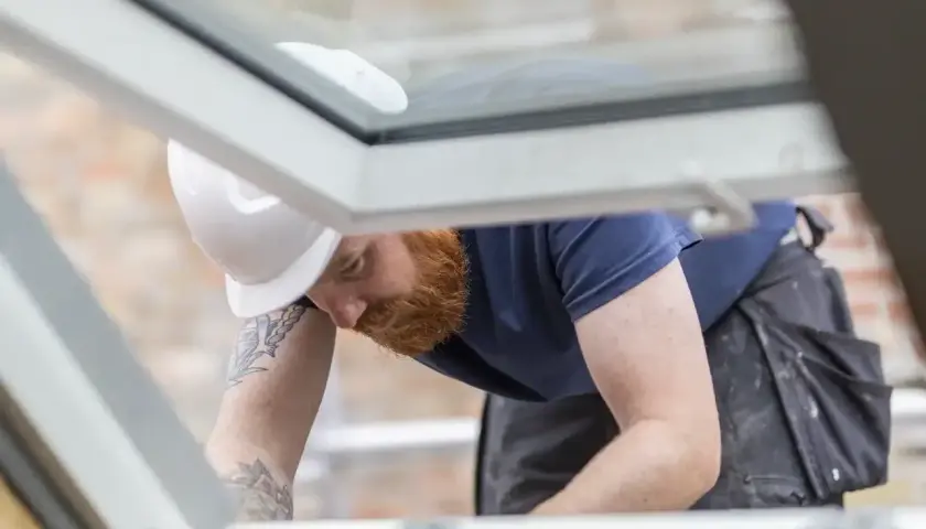 Handwerker mit Bart und Helm dichtet provisorisch das Dach ab.