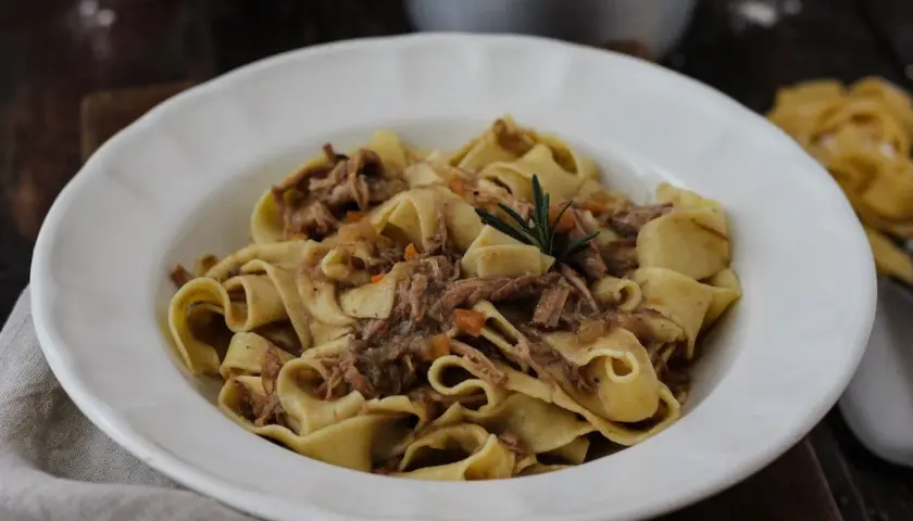Pappardelle con ragù di carne, un classico dei primi piatti di carne, guarnite con rosmarino.
