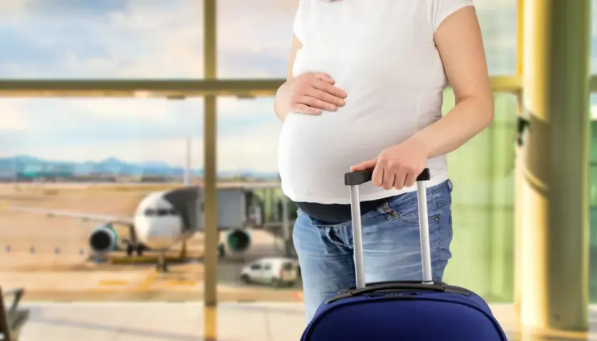 Ciężarna kobieta z walizką na lotnisku, gotowa do podróży. Wygląda na to, że jest fit to fly.
