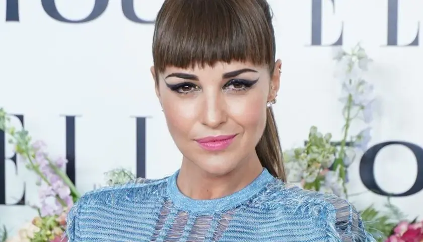Mujer con flequillo recto y maquillaje dramático, luciendo un vestido azul. Explora los diversos tipos de flequillo.