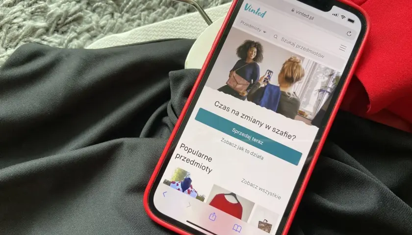 Telefon z aplikacją Vinted leży na ubraniach. Wygląda na to, że portfel Vinted nie działa, bo nie można nic sprzedać.