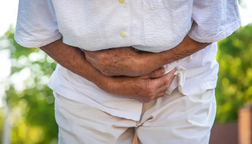 Persona anziana con mani sull'addome, che suggerisce disagio. Potrebbe essere utile sapere cosa prendere per andare in bagno in queste situazioni.