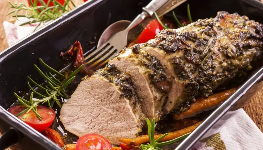 Un délicieux roti de veau aux herbes, servi dans un plat avec des tomates cerises et du romarin.
