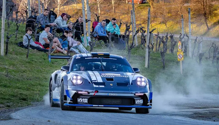 Porsche rast durch das Rebenland bei der Rallye, Zuschauer säumen die Strecke.