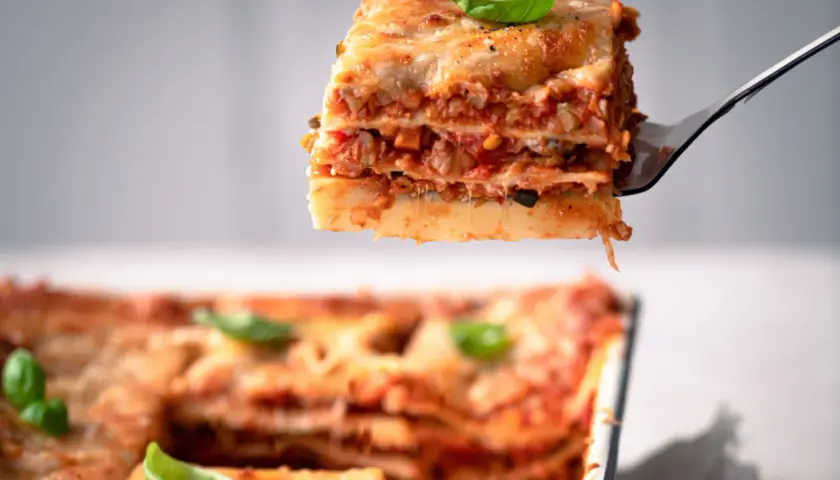 Ein Stück köstliche vegetarische Lasagne wird aus einer Auflaufform gehoben. Frisch, herzhaft und mit Basilikum garniert.