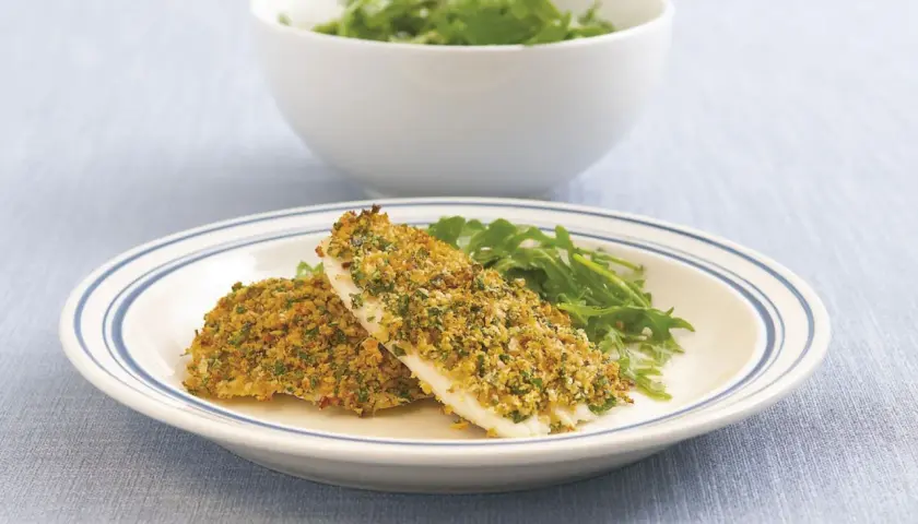 Zwei Filets Fisch mit knuspriger Parmesankruste und Rucola auf einem Teller.