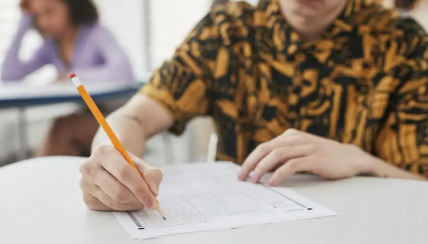 Uczeń pisze ołókiem na arkuszu testowym z wieloma polami wyboru.