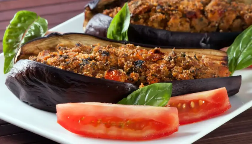 Melanzane ripiene al forno velocissime, dorate e gustose, servite con pomodoro fresco e basilico.