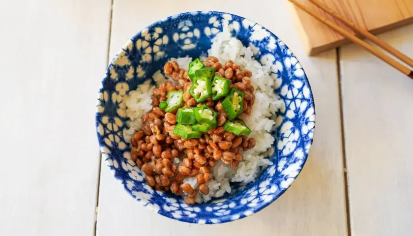 A bowl of natto with rice, topped with sliced okra. This healthy Japanese dish is ready to be enjoyed with chopsticks.