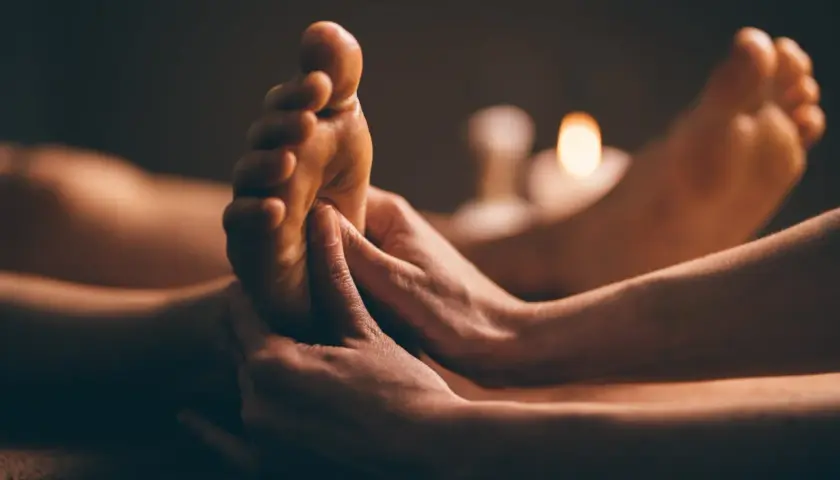 Mains expertes prodiguant un massage plantaire, révélant les bienfaits d'une détente profonde. Bougies tamisées en arrière-plan.