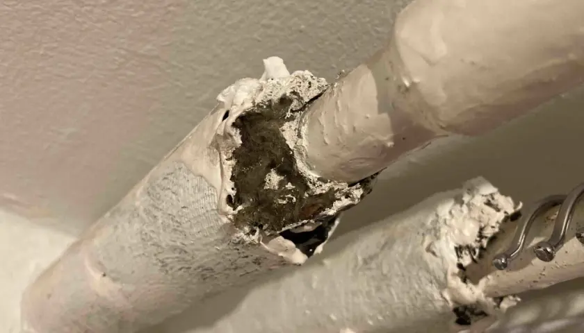 Skadad asbestisolering på rör. Materialet är vitt och smuligt, med synliga fibrer inuti.