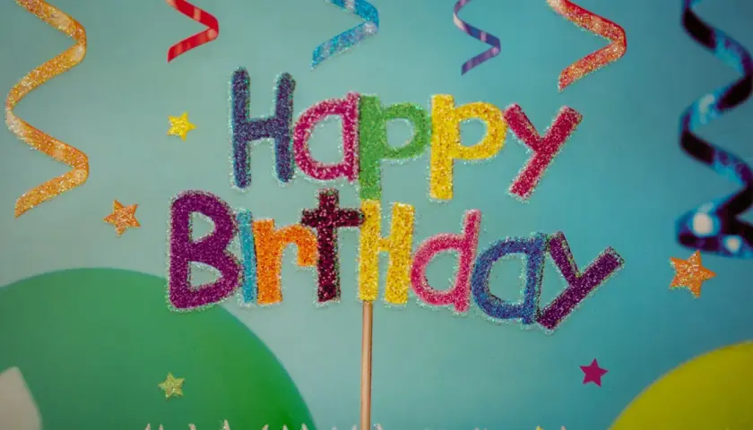 Kolorowe, brokatowe życzenia urodzinowe po angielsku "Happy Birthday" na tle serpentyn i gwiazdek.