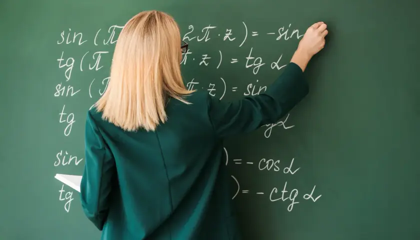 Nauczycielka pisze kredą wzory matematyczne na zielonej tablicy.