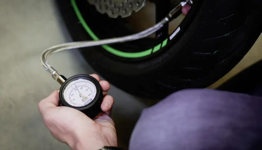 Mano revisando la presión neumaticos moto con un manómetro. El neumático tiene detalles verdes.