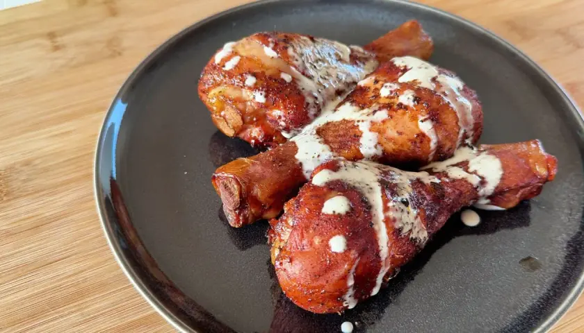 Tre succulenti fusi di pollo arrostiti, conditi con spezie e nappati con una cremosa salsa bianca, serviti su un piatto scuro.