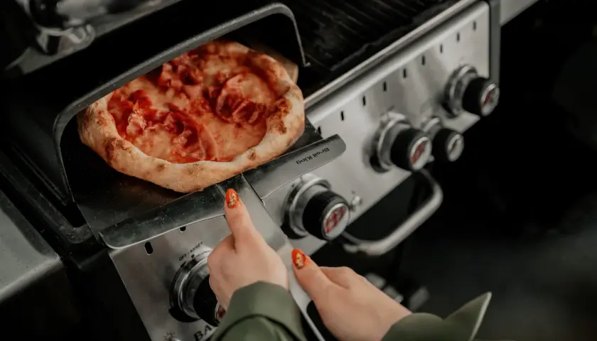 Pizza na grillu, jak piec bez kamienia. Ręka z paznokciem w kształcie pizzy zbliża się do gorącego dania.