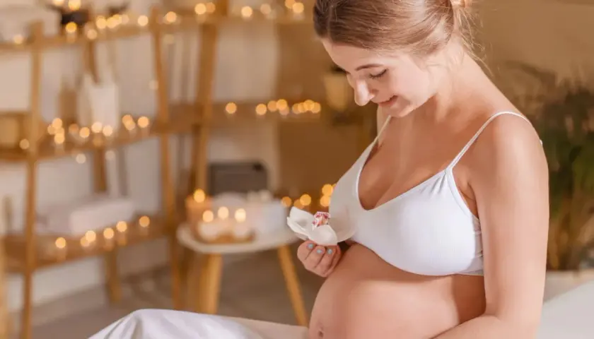 Uśmiechnięta ciężarna kobieta trzyma kwiat. Delikatne światła tworzą atmosferę relaksu, idealną dla kosmetyków dla kobiet w ciąży.