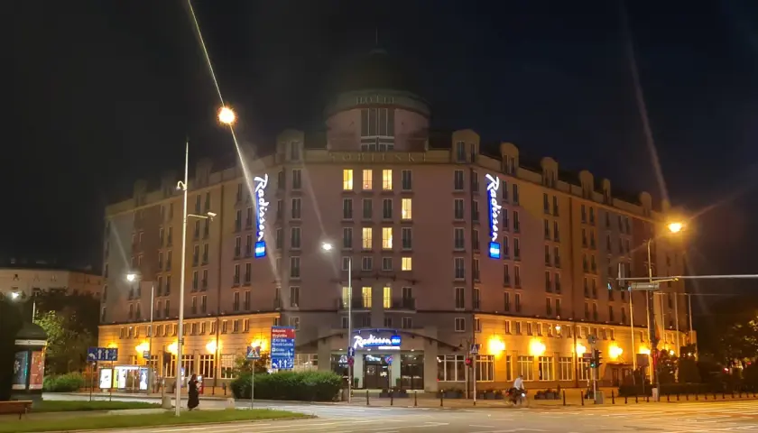Nocą oświetlony Radisson Blu Sobieski Hotel Warsaw z neonami "Radisson" i napisem "HOTEL SOBIESKI".