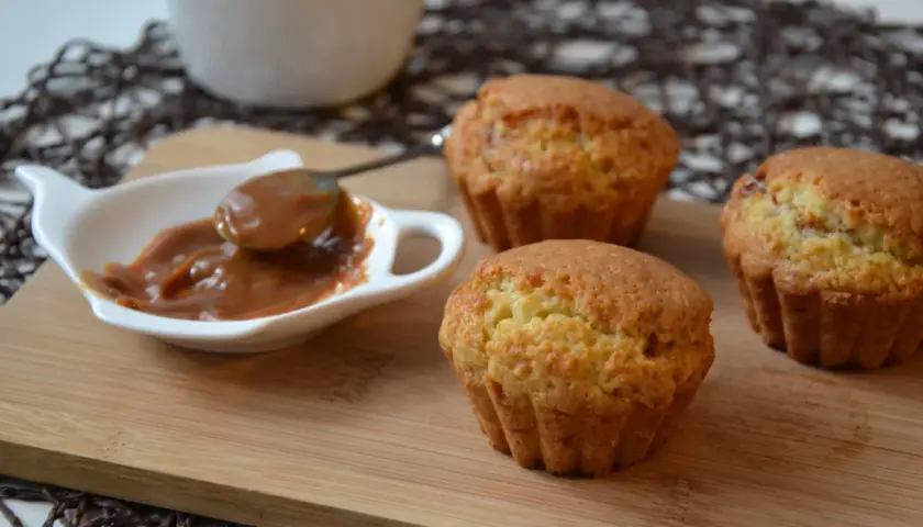 Trzy muffiny z toffifee na desce, obok sos karmelowy w białej miseczce.
