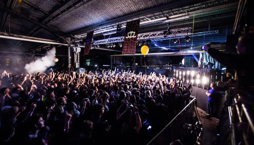 Stor publik under bron på en konsert, med ljus och rök som skapar en festlig stämning.