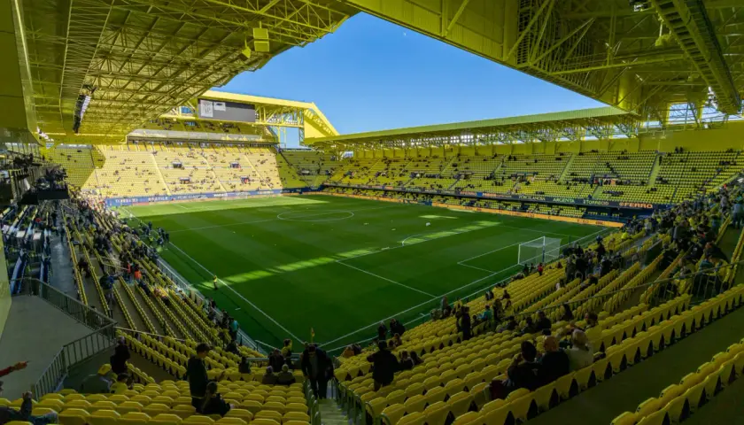 Stadion Villarreal, wypełniony żółtymi siedzeniami, z zieloną murawą i błękitnym niebem.