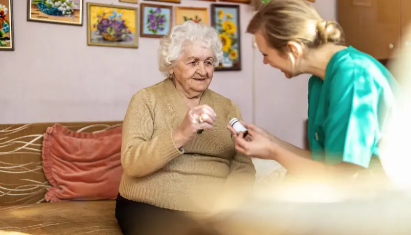 Pflegekraft reicht einer älteren Dame Medikamente für die Obstipationsprophylaxe.