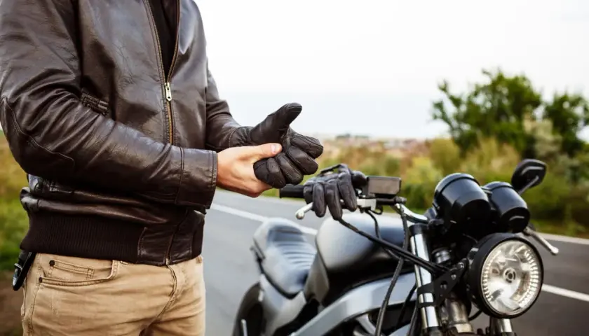 Hombre con chaqueta de cuero se pone guantes junto a una moto. ¿Listo para vender moto sin papeles?