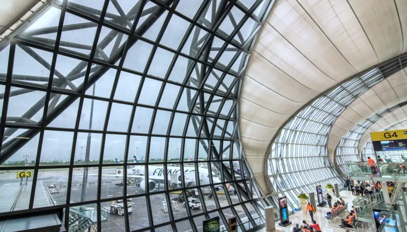 Moderne Architektur am Flughafen Bangkok: Flugzeuge stehen bereit, während Reisende im Wartebereich auf ihren Abflug warten.