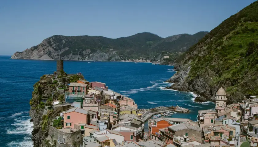 Colorful houses cling to the cliffs of the Cinque Terre Italy coast, overlooking a vibrant blue sea. A medieval tower stands guard.