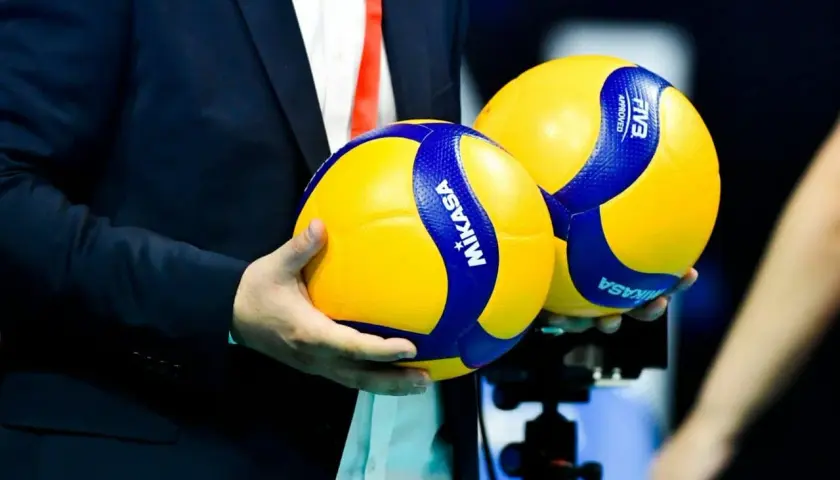 Dwie piłki do siatkówki Mikasa w rękach mężczyzny w garniturze. Czy wiesz, do ilu setów gra się w siatkówce?