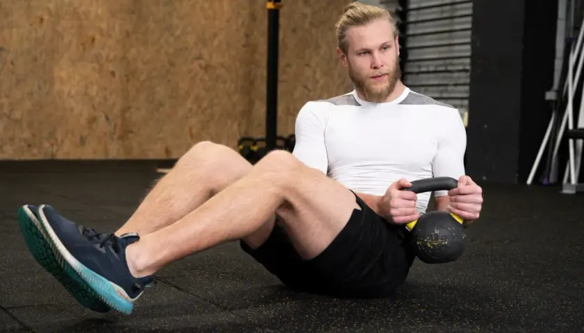 Mężczyzna wykonuje brzuszki z obciążeniem, trzymając kettlebell.