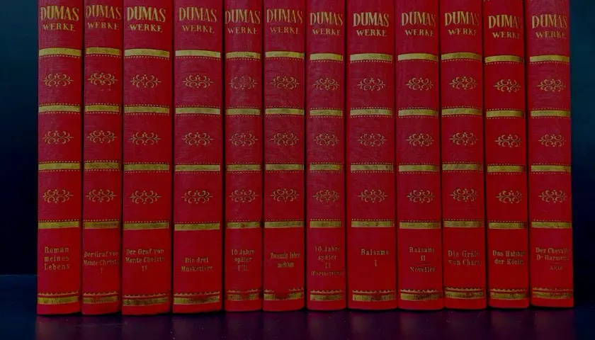 Eine Reihe roter Bücher mit goldener Verzierung, die Werke von Alexandre Dumas dem Älteren enthalten.