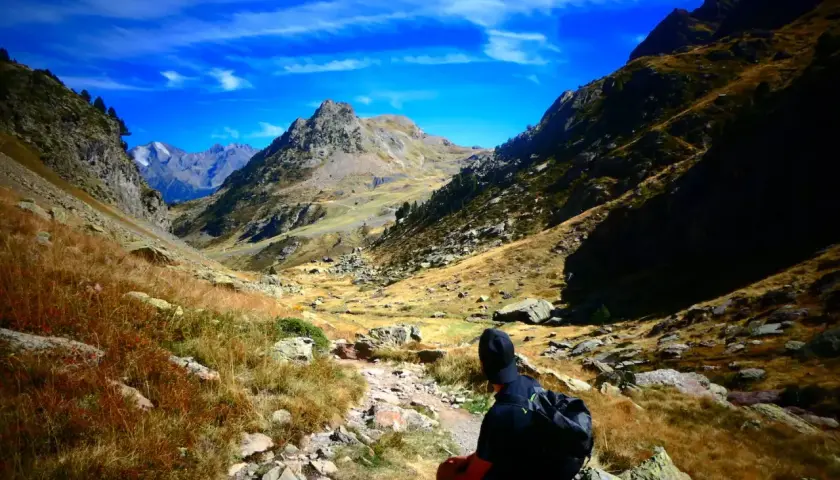 Senderista contempla la inmensidad de los montes Pirineos bajo un cielo azul intenso.
