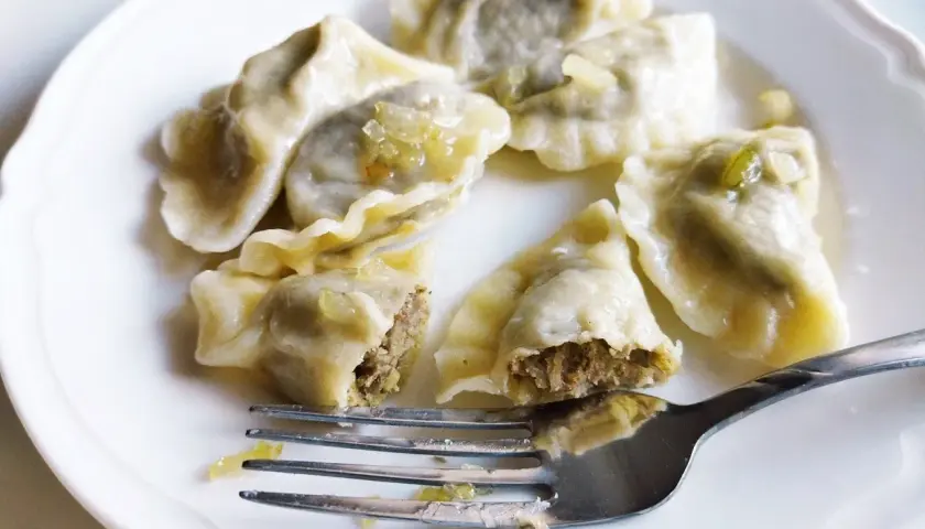 Pyszne pierogi z soczewicą na białym talerzu, jeden nadgryziony, obok widelec.