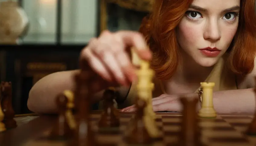 Anya Taylor-Joy jako Beth Harmon w "Gambicie Królowej" wykonuje ruch figurą na szachownicy.