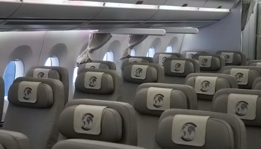 Innenansicht eines Flugzeugs mit Reihen von grauen Sitzen, die für den Bundeskanzler und seine Delegation reserviert sind. Jede Kopfstütze ziert ein Emblem mit der Weltkugel.