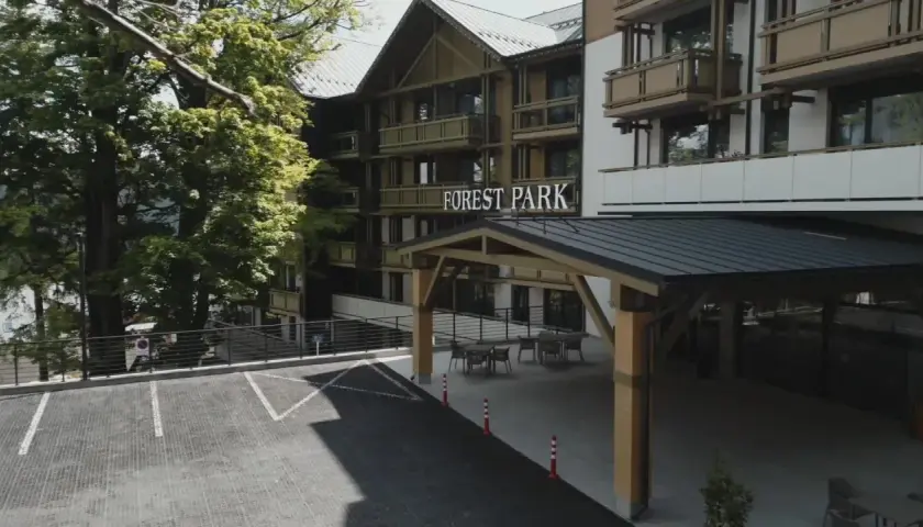 Elegancki hotel 5 gwiazdkowy Forest Park otoczony zielenią, z parkingiem i zadaszonym wejściem.