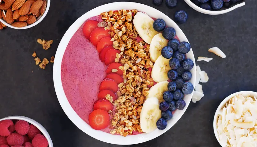 En färgglad acai bowl med jordgubbar, banan, blåbär och granola. Serveras med mandlar och kokosflingor.