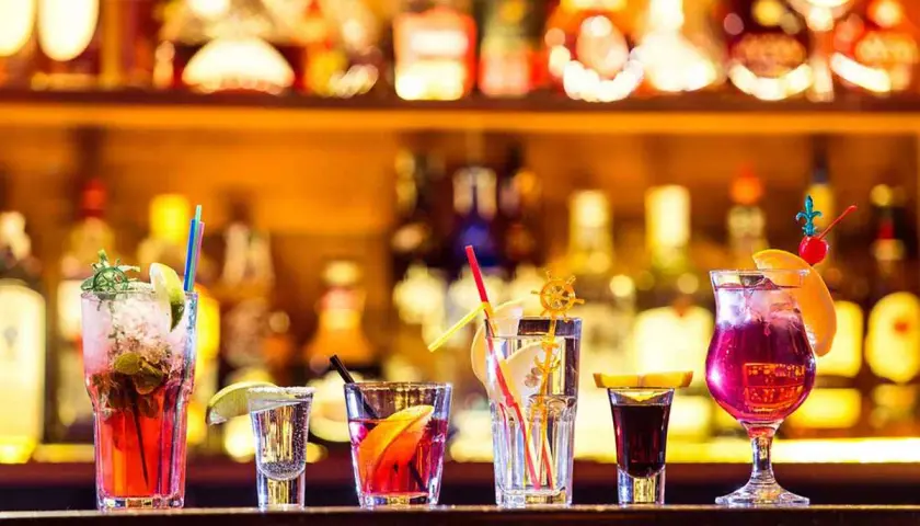 Varietà di cocktail principali colorati e rinfrescanti, guarniti con frutta e cannucce, su uno sfondo di bottiglie illuminate.