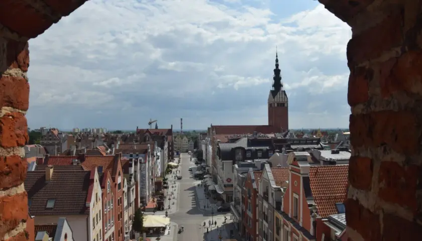Widok na ulicę i kamienice w **starym mieście Elbląg**. W oddali widać wieżę kościoła.