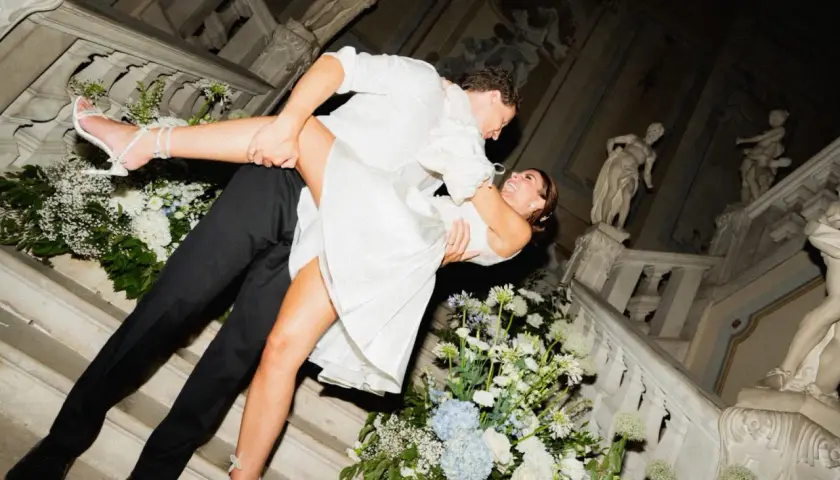 Un couple s'embrasse passionnément lors de leur mariage chez soi, entouré de fleurs blanches et bleues sur un escalier orné de statues.