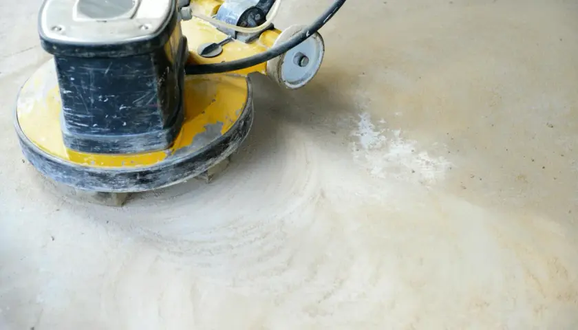 Eine Poliermaschine bearbeitet einen geschliffenen Betonboden, hinterlässt feinen Staub und glatte Spuren.