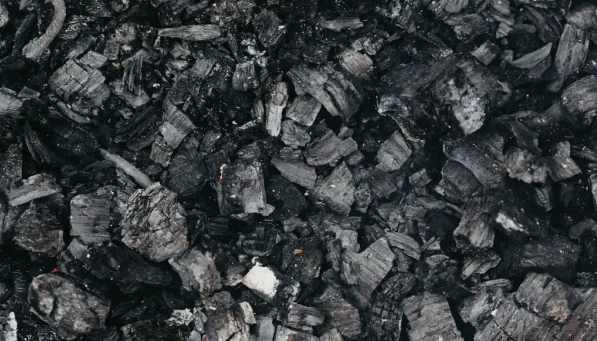 Gros plan sur des morceaux de machefer pellet, résidus noirs et gris de combustion, évoquant la chaleur d'un feu de bois.