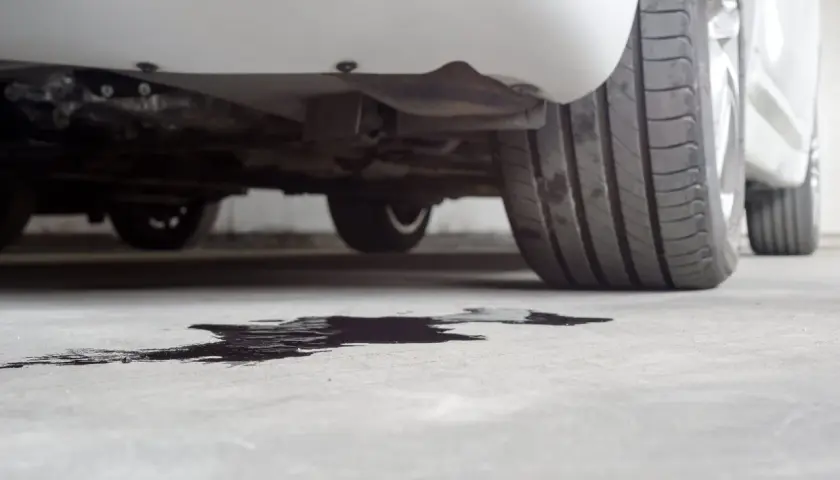 Macchia scura sul cemento sotto un'auto, probabile perdita liquido radiatore.
