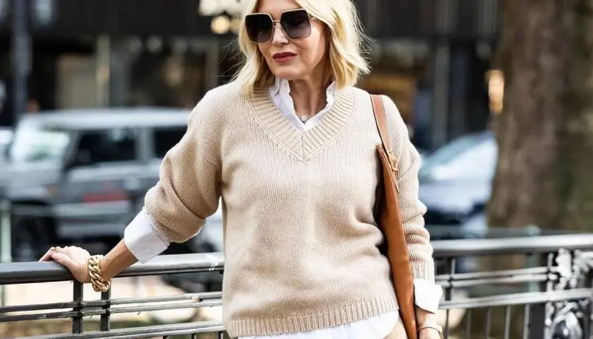 Elegancka kobieta po 50-tce w beżowym swetrze i białej koszuli. Stylowa moda dla 50 latki.