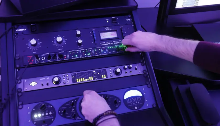 Main d'un ingénieur du son ajustant les potentiomètres d'un rack d'équipement audio, en pleine action de mastering musique.