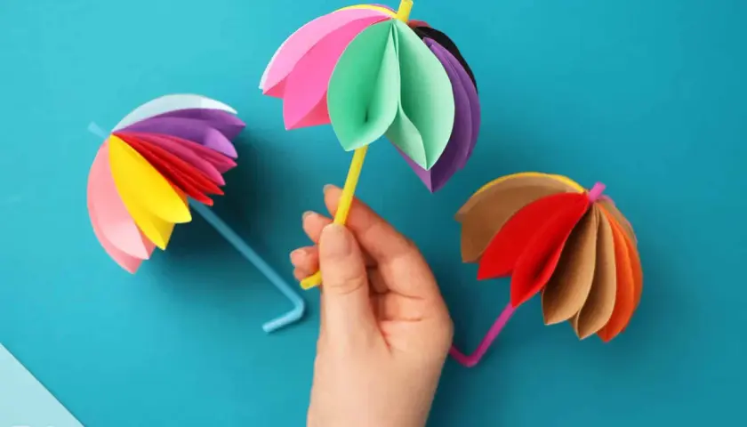 Bunte Papier-Regenschirme, die zum **Regenschirm basteln einfach** einladen. Ein gelber Strohhalm hält einen bunten Schirm.