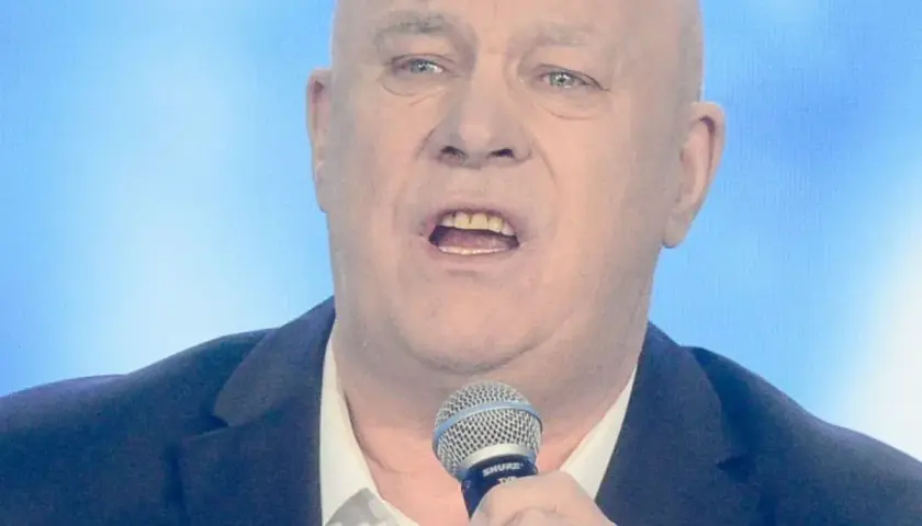 Ryszard Rynkowski śpiewa, trzymając mikrofon. Jego charakterystyczne utwory poruszają serca słuchaczy.